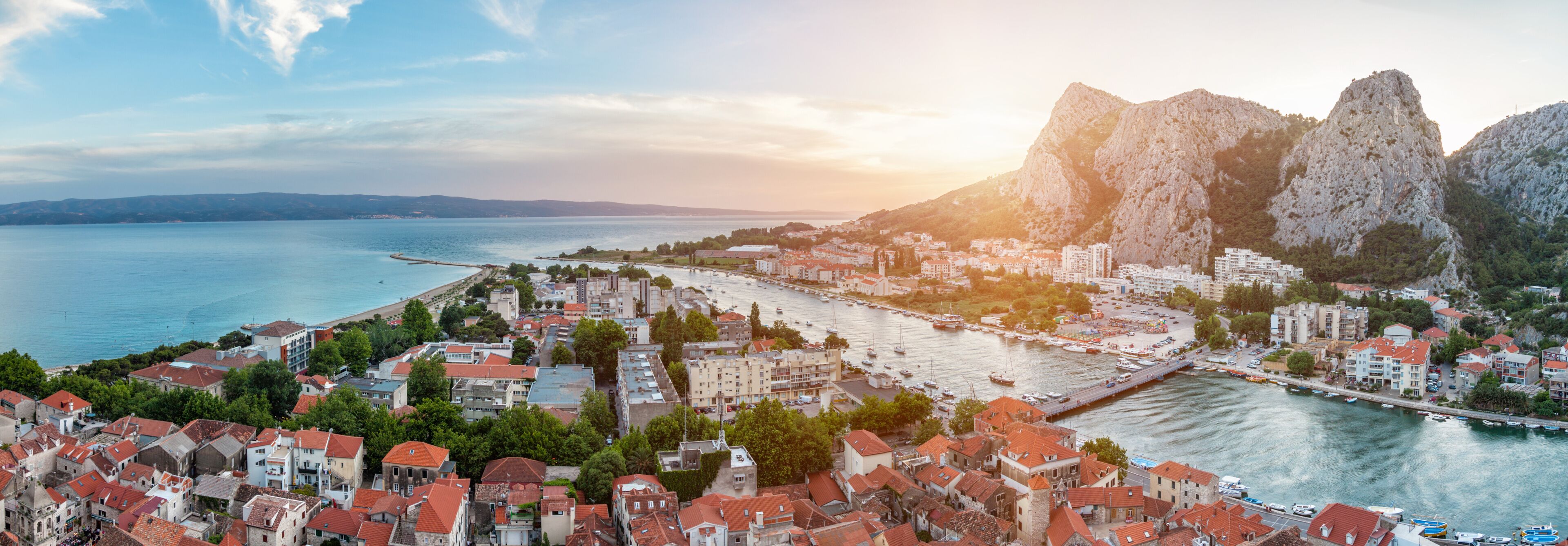 A coastal town with red-roofed buildings, a marina, and rocky cliffs.