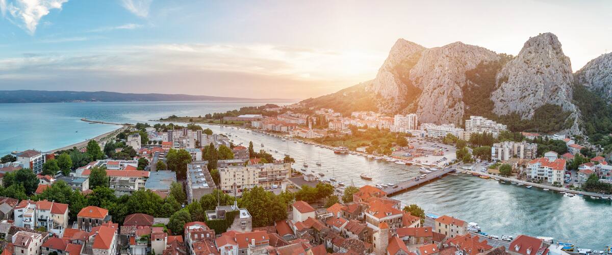 A coastal town with red-roofed buildings, a marina, and rocky cliffs.