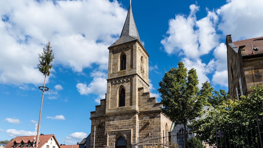 Eine historische Kirche mit einem hohen Kirchturm und einer Turmuhr, umgeben von Bäumen und Gebäuden.