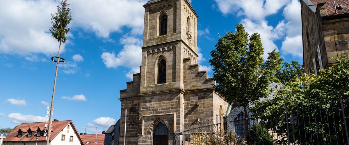 A historic church with a tall steeple and clock tower, surrounded by trees and buildings.