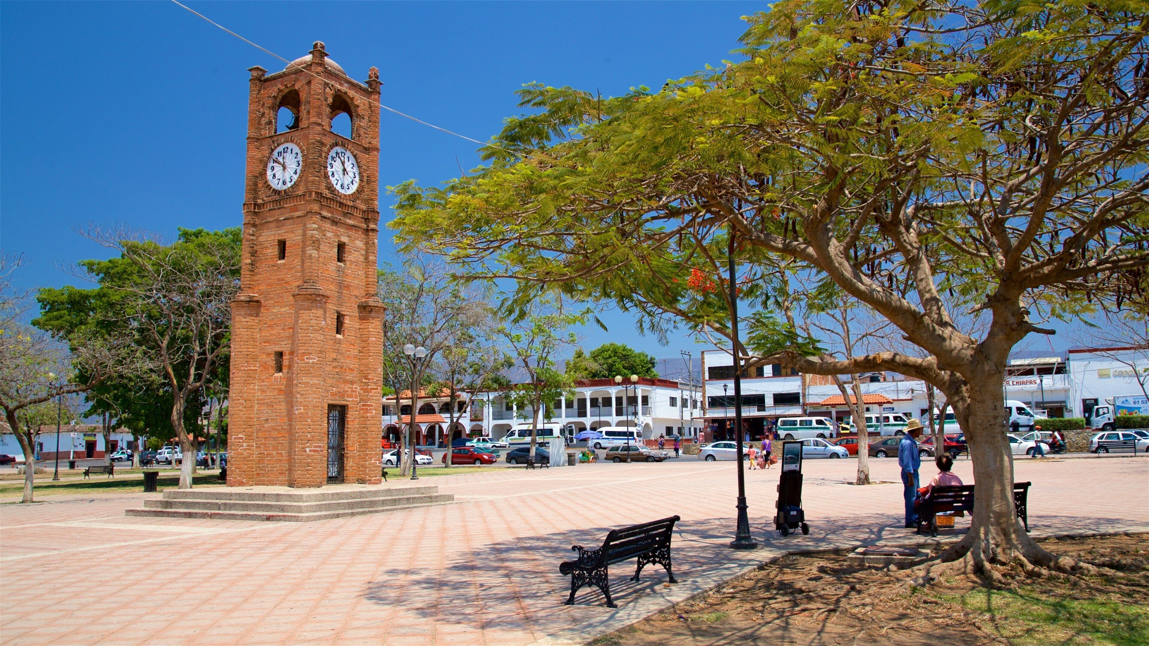A clock tower, a park with benches, and a busy street with cars and buildings.