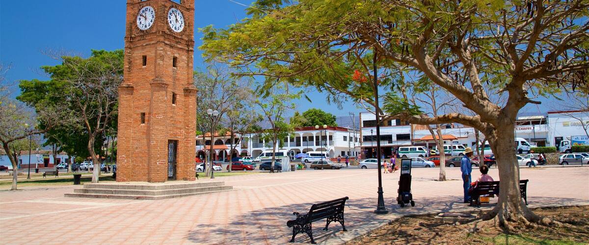 A clock tower, a park with benches, and a busy street with cars and buildings.