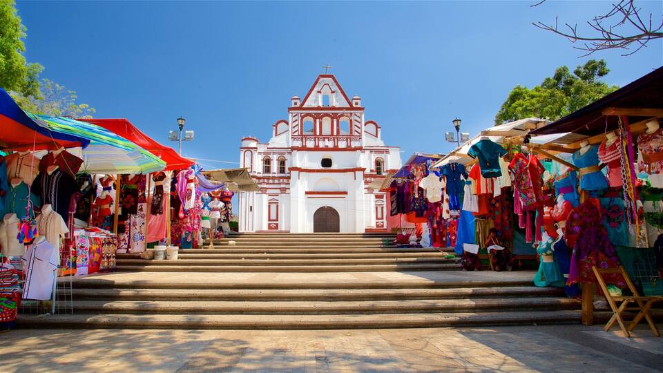 A market street with colorful stalls and a white church with red trim in the background.