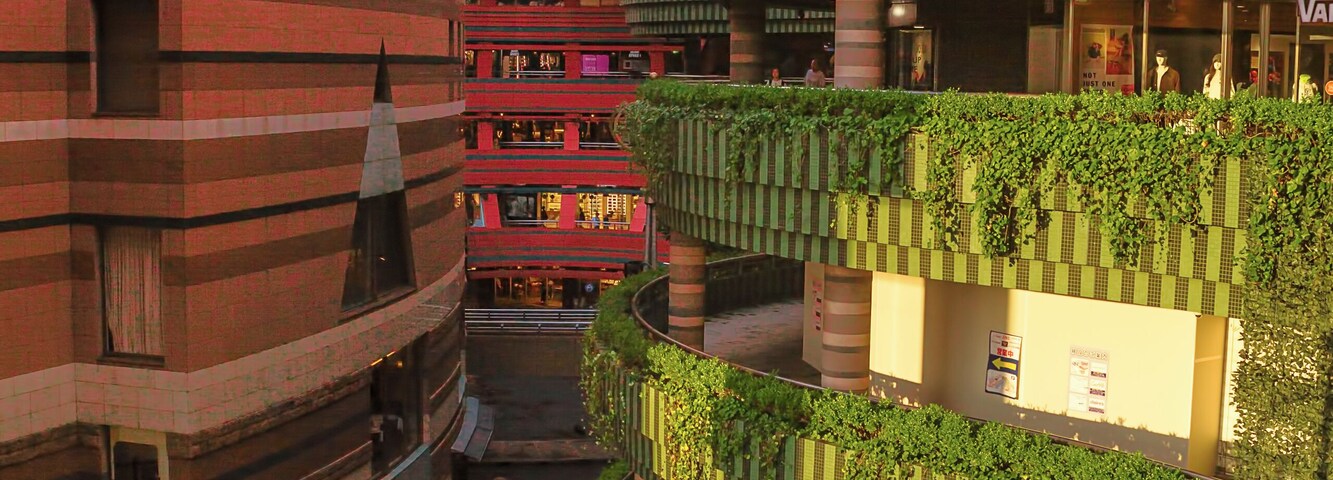 Um complexo urbano com vários níveis, plantas trepadeiras verdes, um edifício vermelho e uma placa da United Cinemas.
