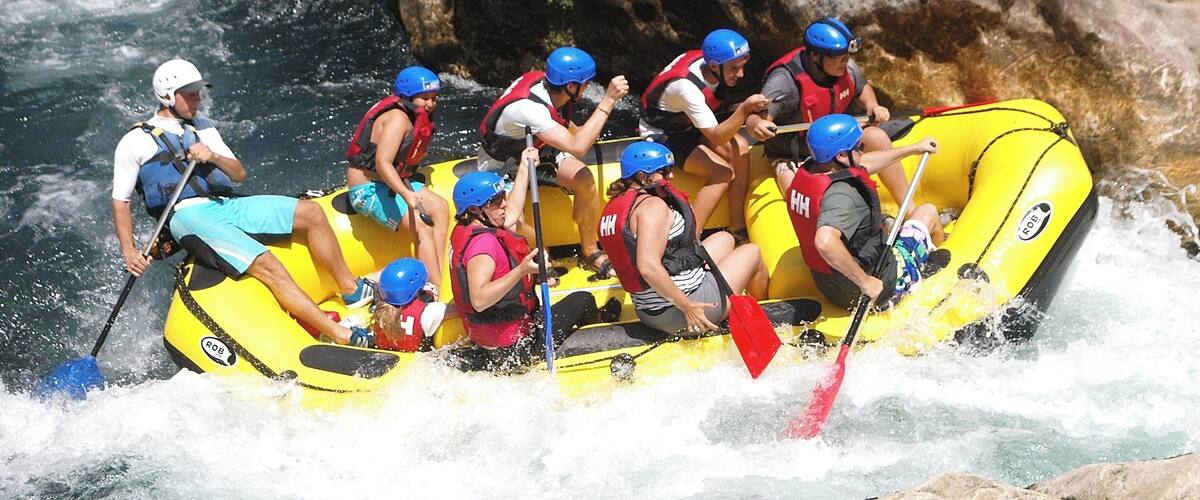 A group of people in a yellow raft navigating a river with rapids, surrounded by large rocks and greenery.