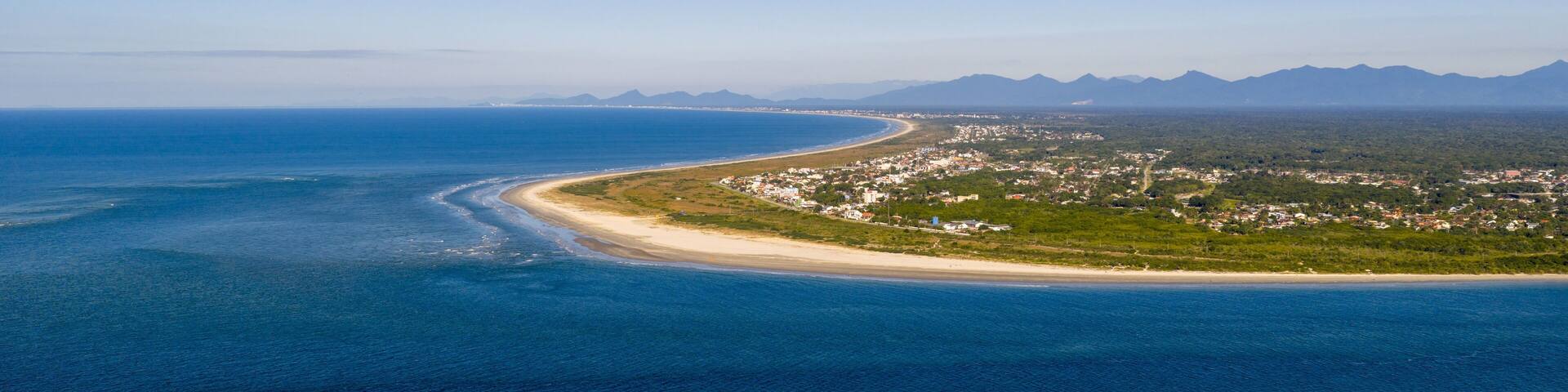 Aerial view of Pontal do Sul, Paraná, Brazil, showing a long coastline with blue ocean and green land.
