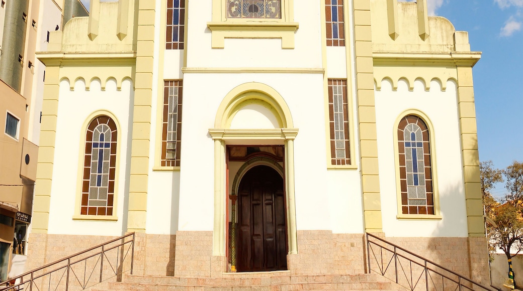 A church with a white facade, a clock, and a cross on top.