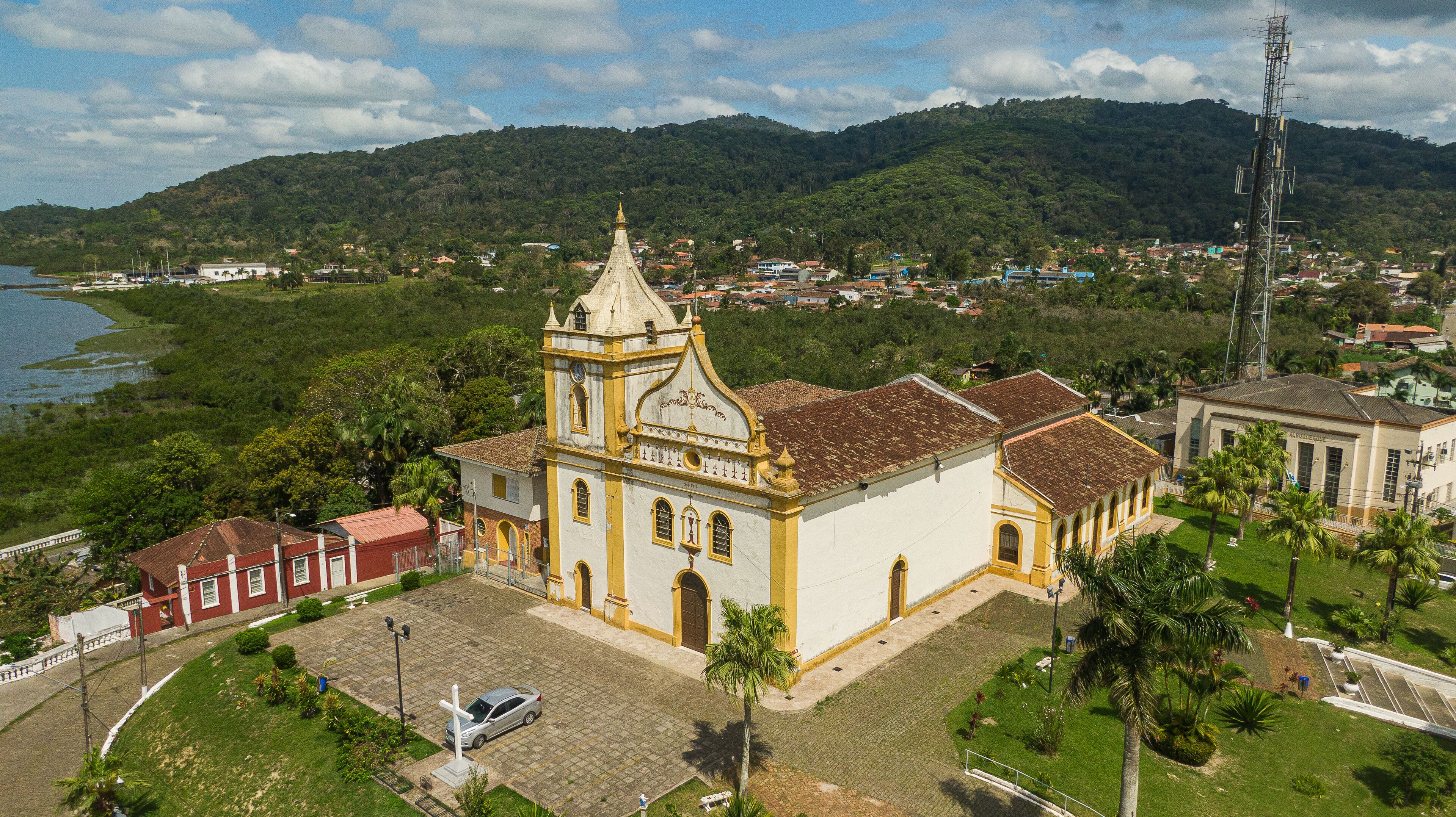 A church with a bell tower, surrounded by greenery and a lake.