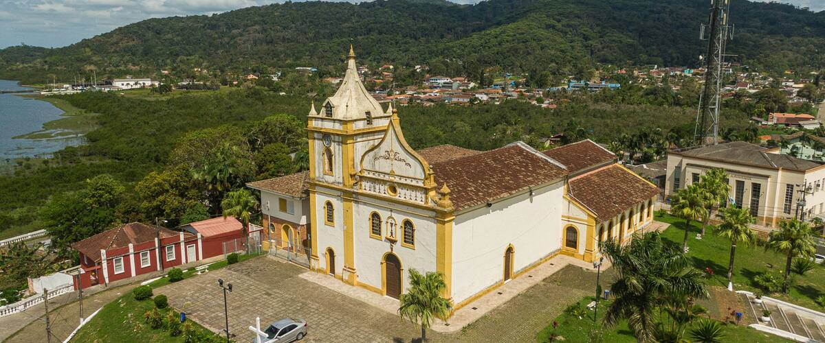 A church with a bell tower, surrounded by greenery and a lake.