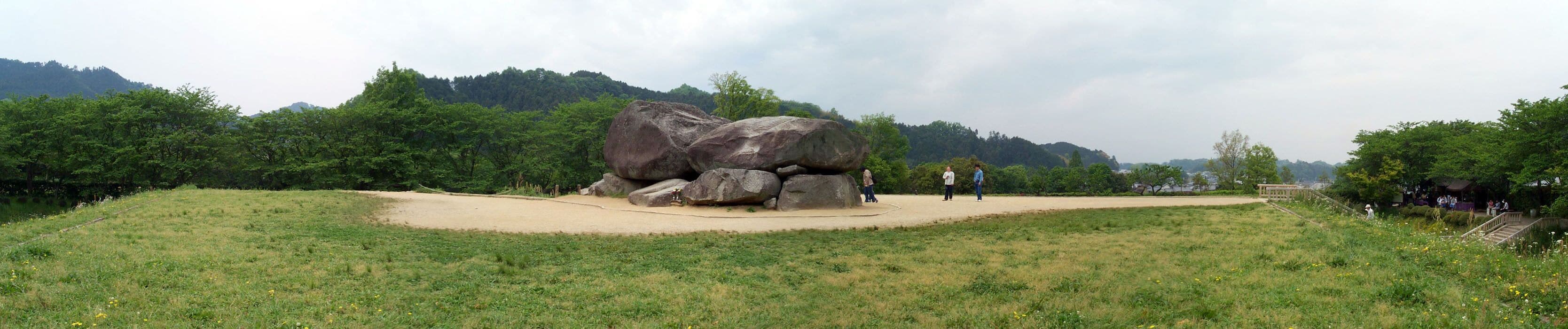 A large rock formation in a park with a dirt path and greenery.