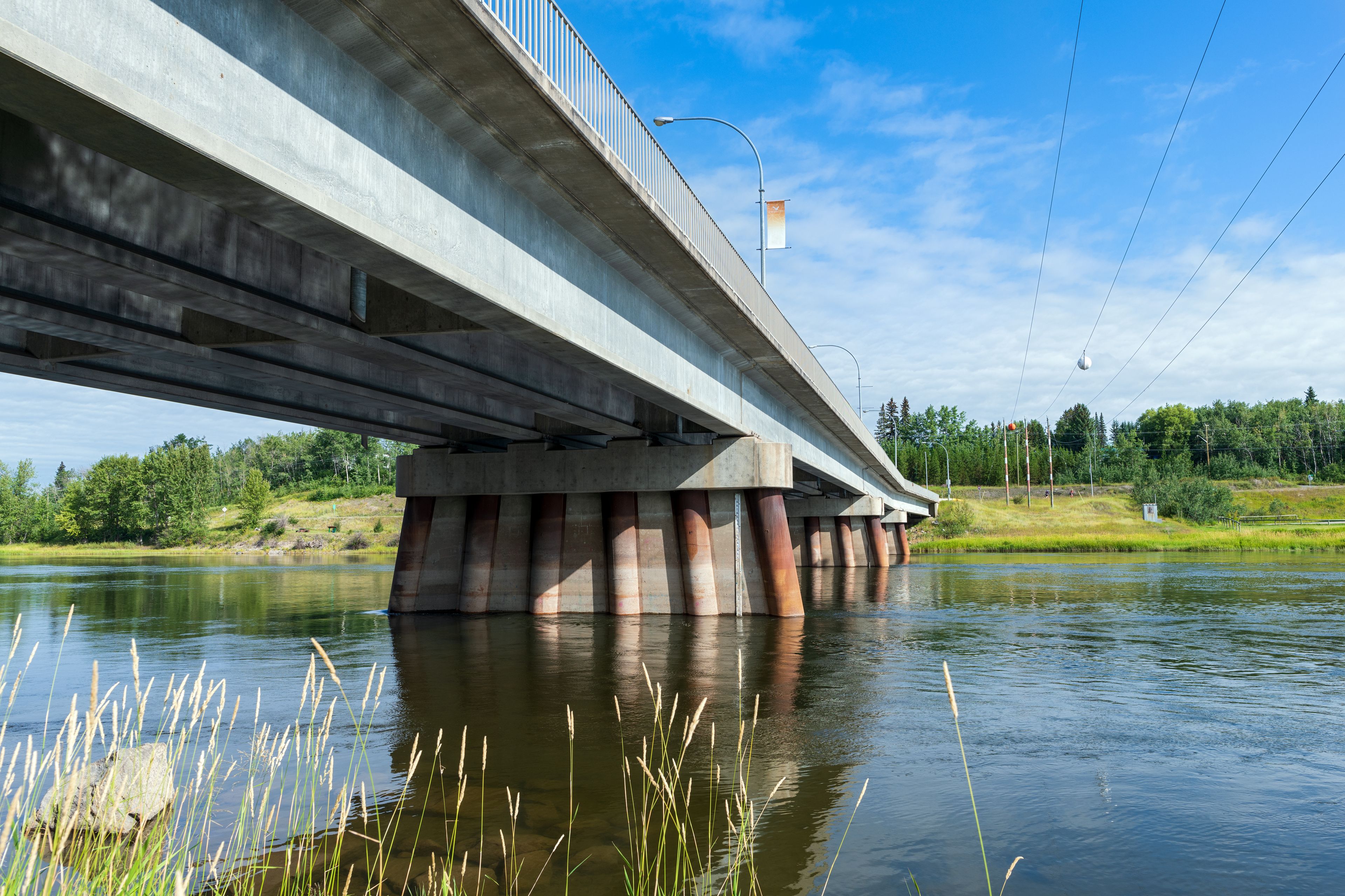 A concrete bridge over a calm river with grass and trees in the background.
