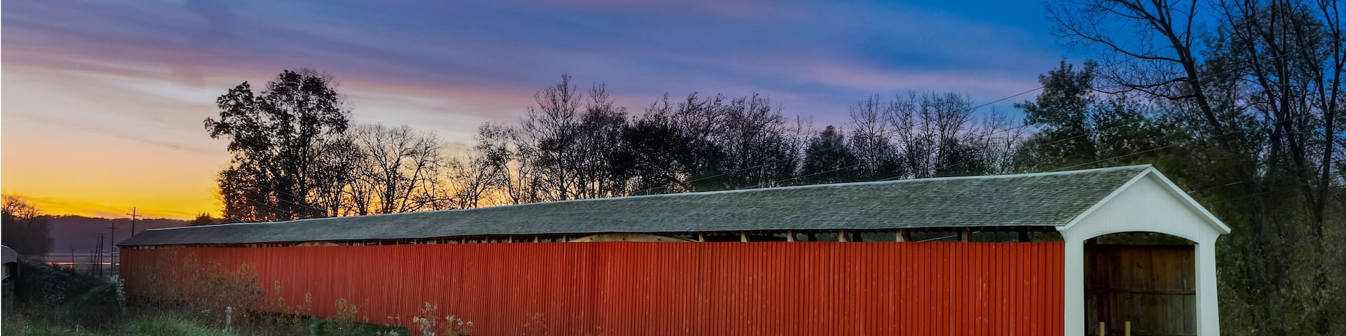 A red covered bridge with a white roof, surrounded by grassy fields and trees.