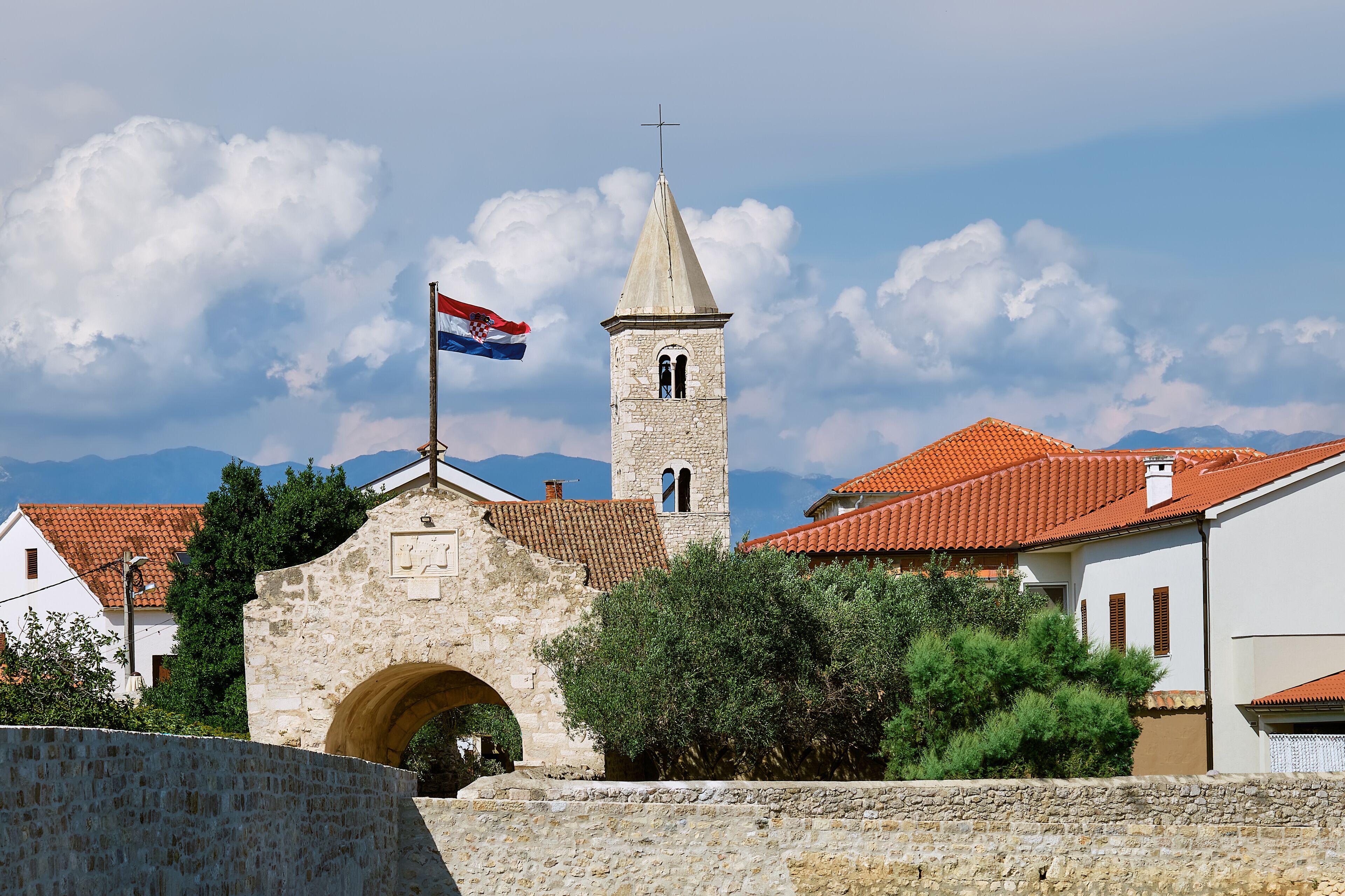 A stone tower with a flag, a red-tiled roof building, and a stone archway.