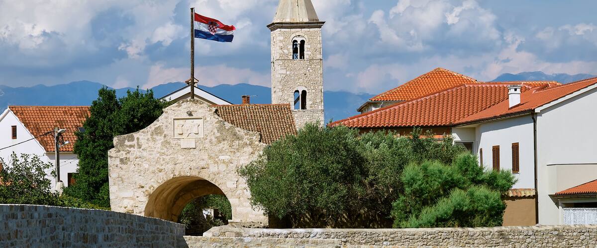 A stone tower with a flag, a red-tiled roof building, and a stone archway.