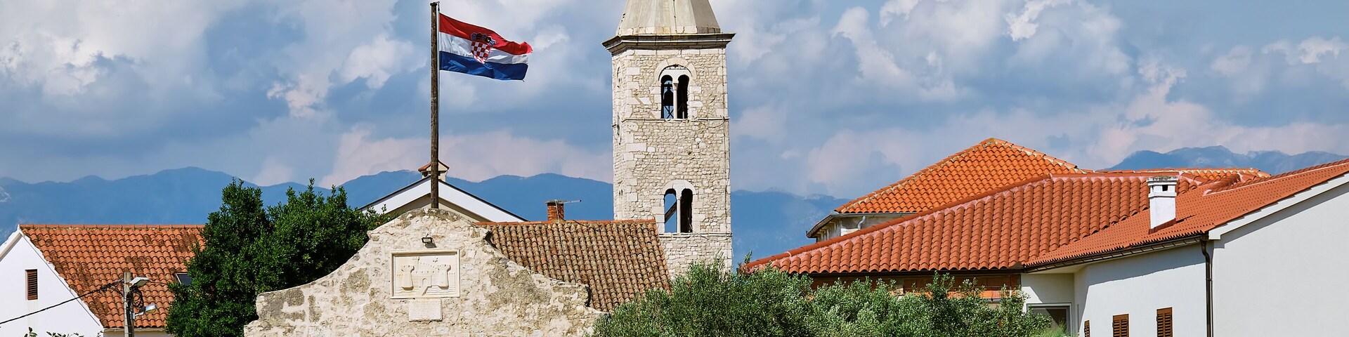 A stone tower with a flag, a red-tiled roof building, and a stone archway.