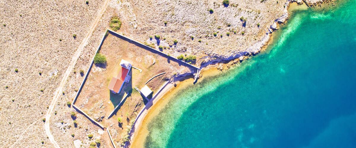 An aerial view of a coastal area with a rectangular structure, a narrow path, and clear turquoise waters.