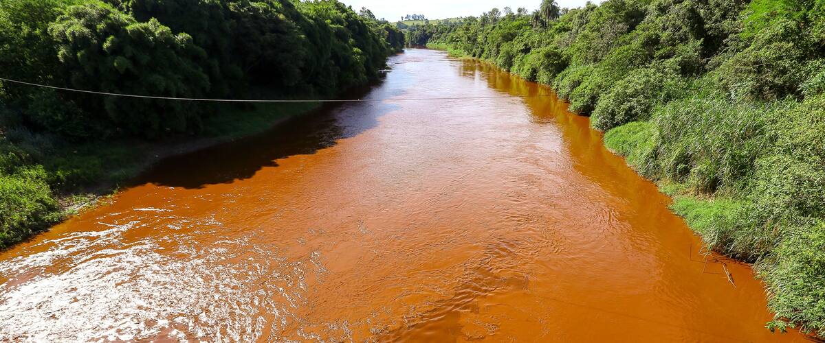 A river with reddish-brown water flowing through a green landscape.