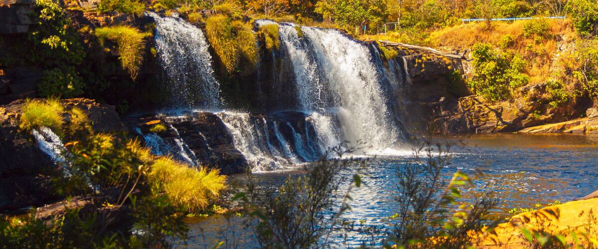 A waterfall cascading into a river surrounded by lush greenery and rocky terrain.