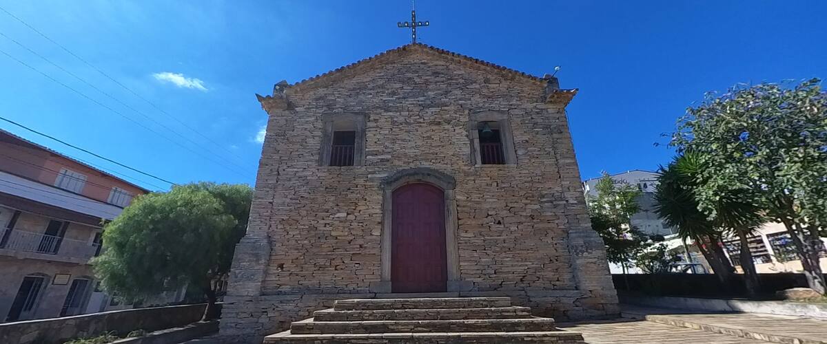 A stone church with a red door and a cross on top, surrounded by trees and buildings.