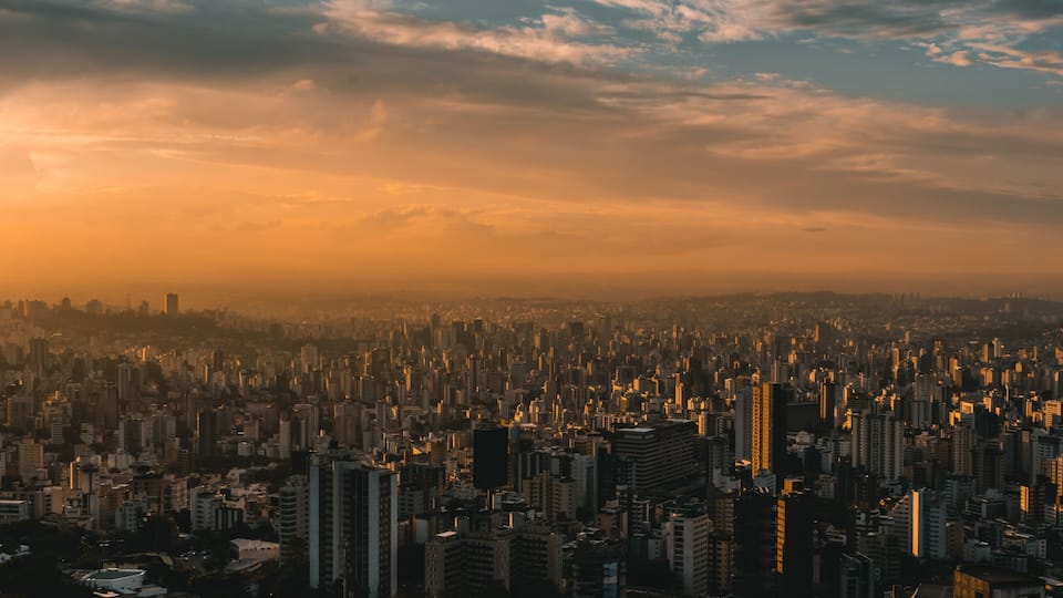 A cityscape at sunset with dense urban buildings and a hazy sky.