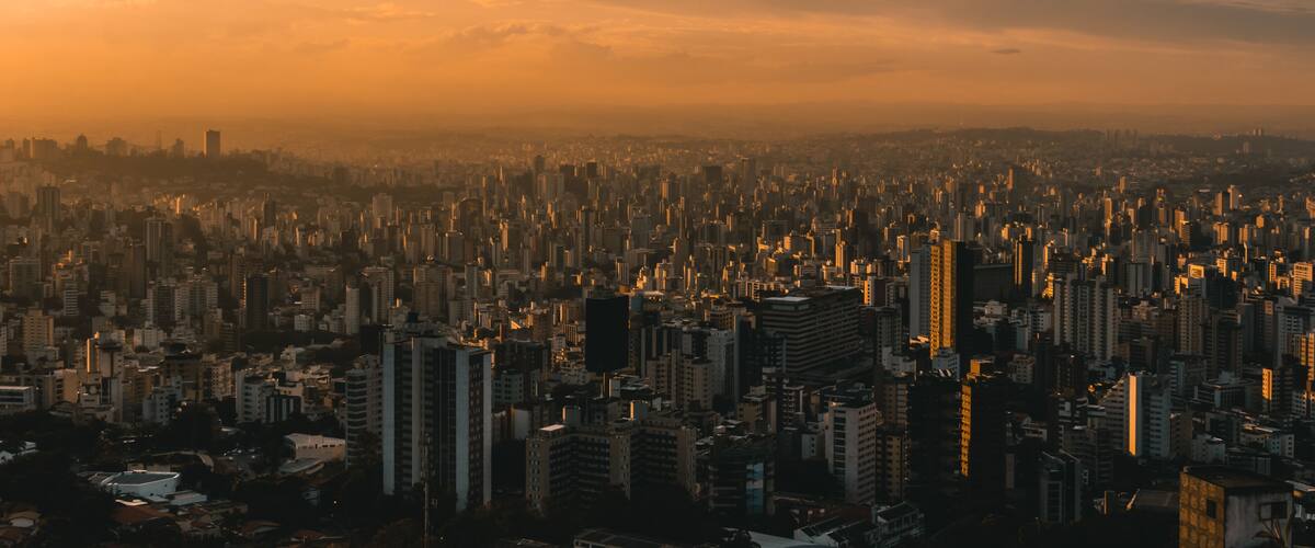 A cityscape at sunset with dense urban buildings and a hazy sky.