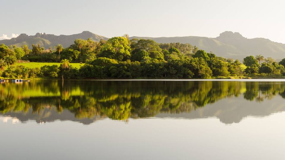 A calm lake reflecting trees and mountains.