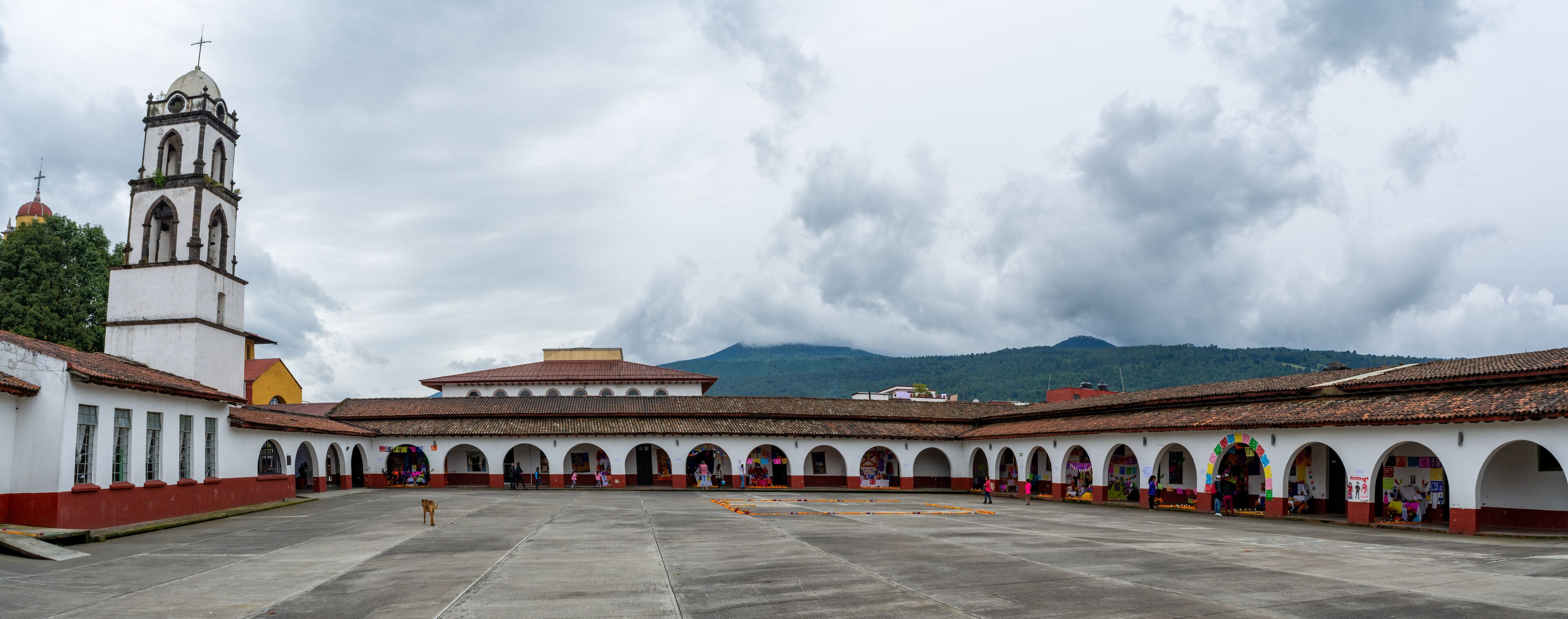A courtyard with a bell tower, arches, and a mountain in the background.