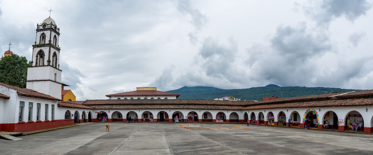 A courtyard with a bell tower, arches, and a mountain in the background.