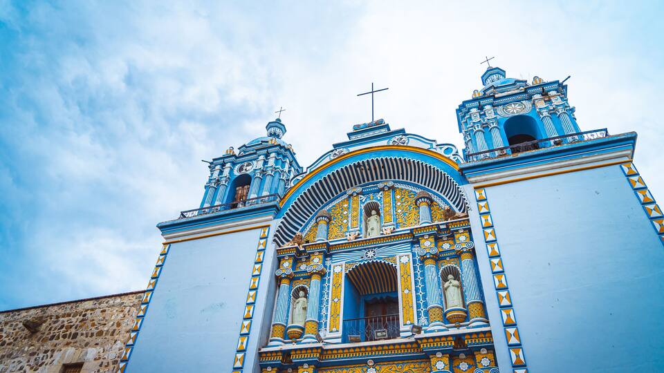 A colorful church with intricate blue and gold patterns, two bell towers, and a cross on top.