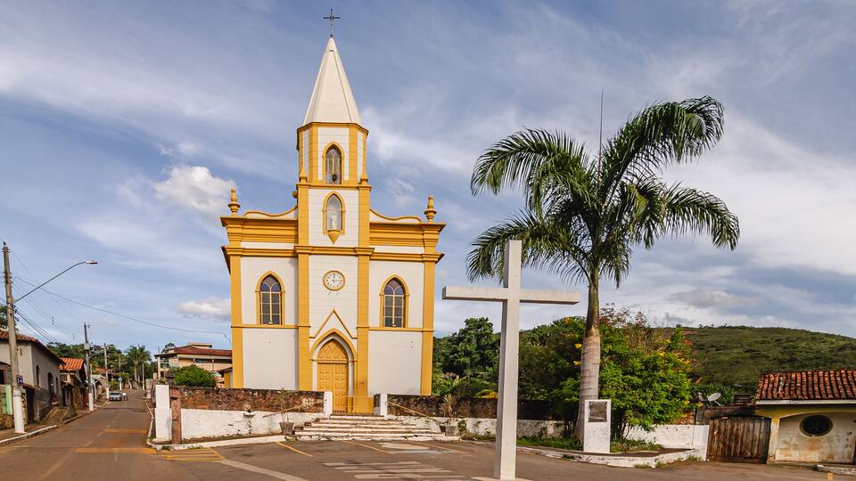 A yellow church with a bell tower and a palm tree in front.