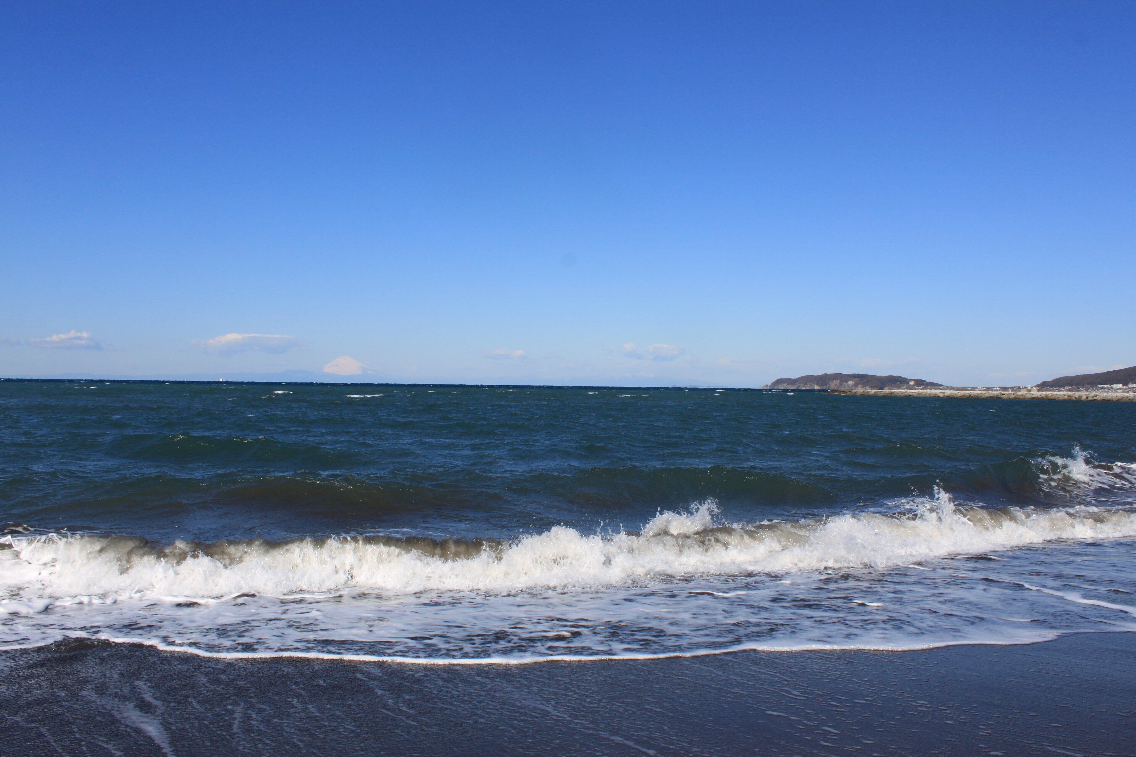 A beach with waves crashing onto the shore under a clear blue sky.