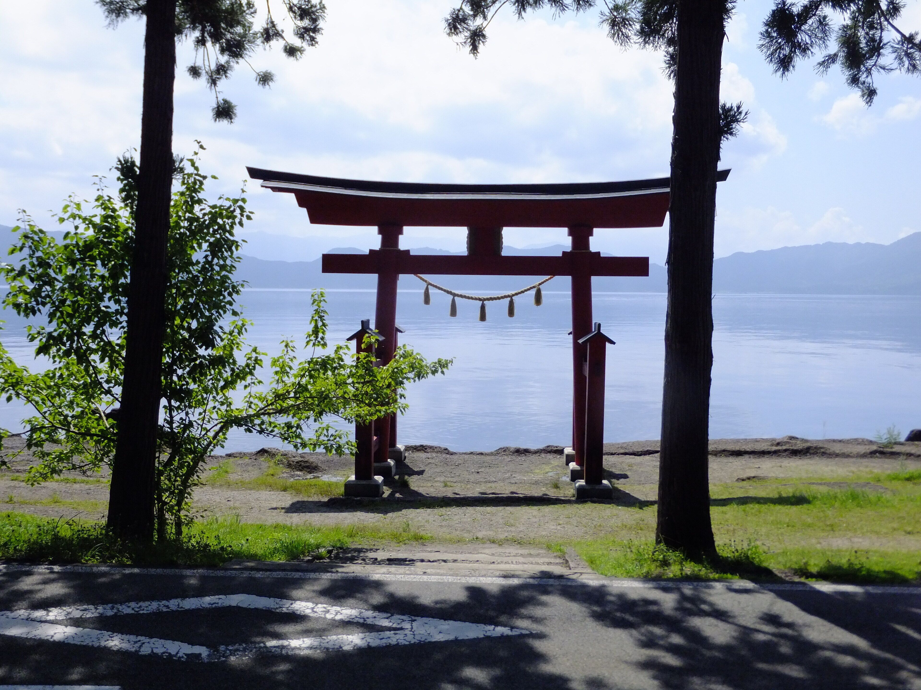Un torii a la entrada de un santuario, con vistas a un lago tranquilo y montañas al fondo.