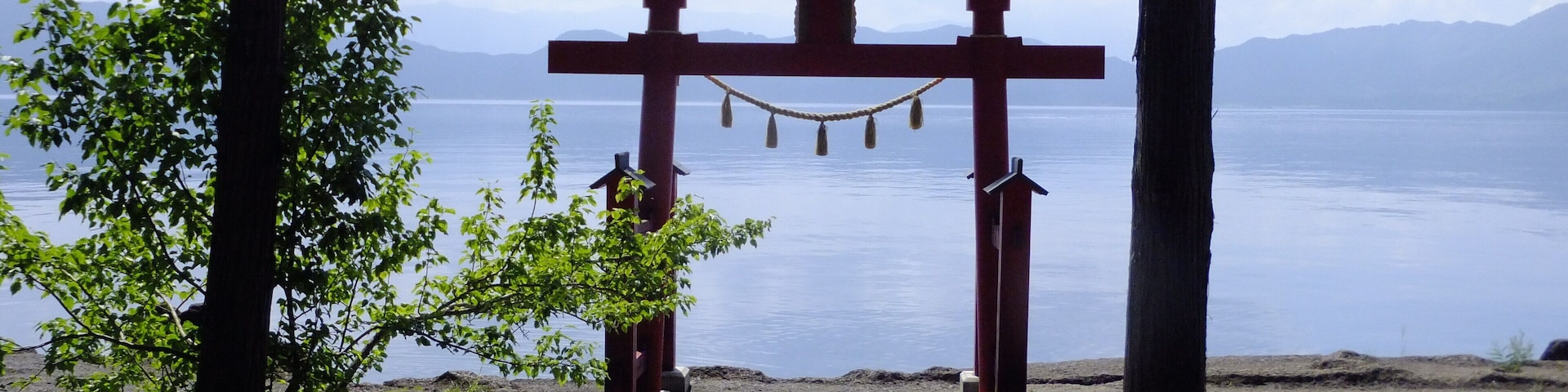 Un torii a la entrada de un santuario, con vistas a un lago tranquilo y montañas al fondo.