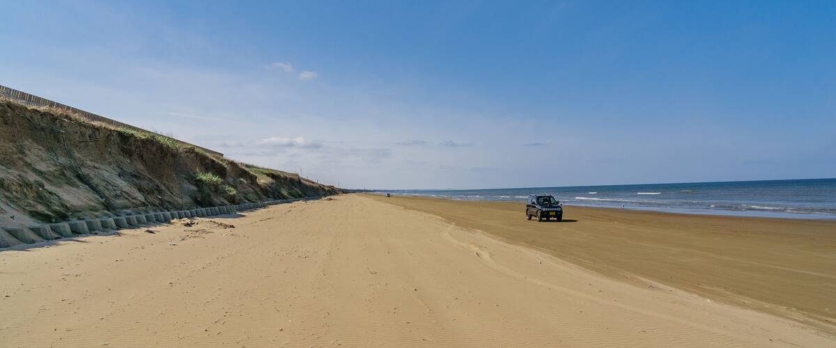 A sandy beach with a dune and a vehicle on the right.