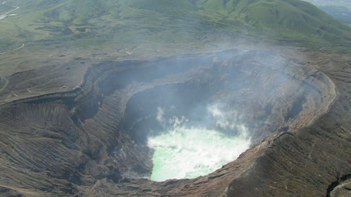 Mount Aso acid lake (crater of Mount Naka) seen from helicopter. Green mountains in the background, in the NW direction, are Mounts Kijima (left) and Ojo (right). Aso caldera walls are also visible further back. The picture points to the NW direction.