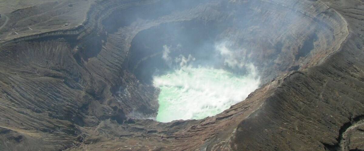 A large crater with a greenish lake surrounded by green hills.