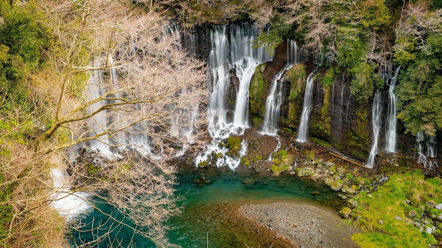 A multi-tiered waterfall cascading into a clear turquoise pool surrounded by lush greenery and rocky terrain.