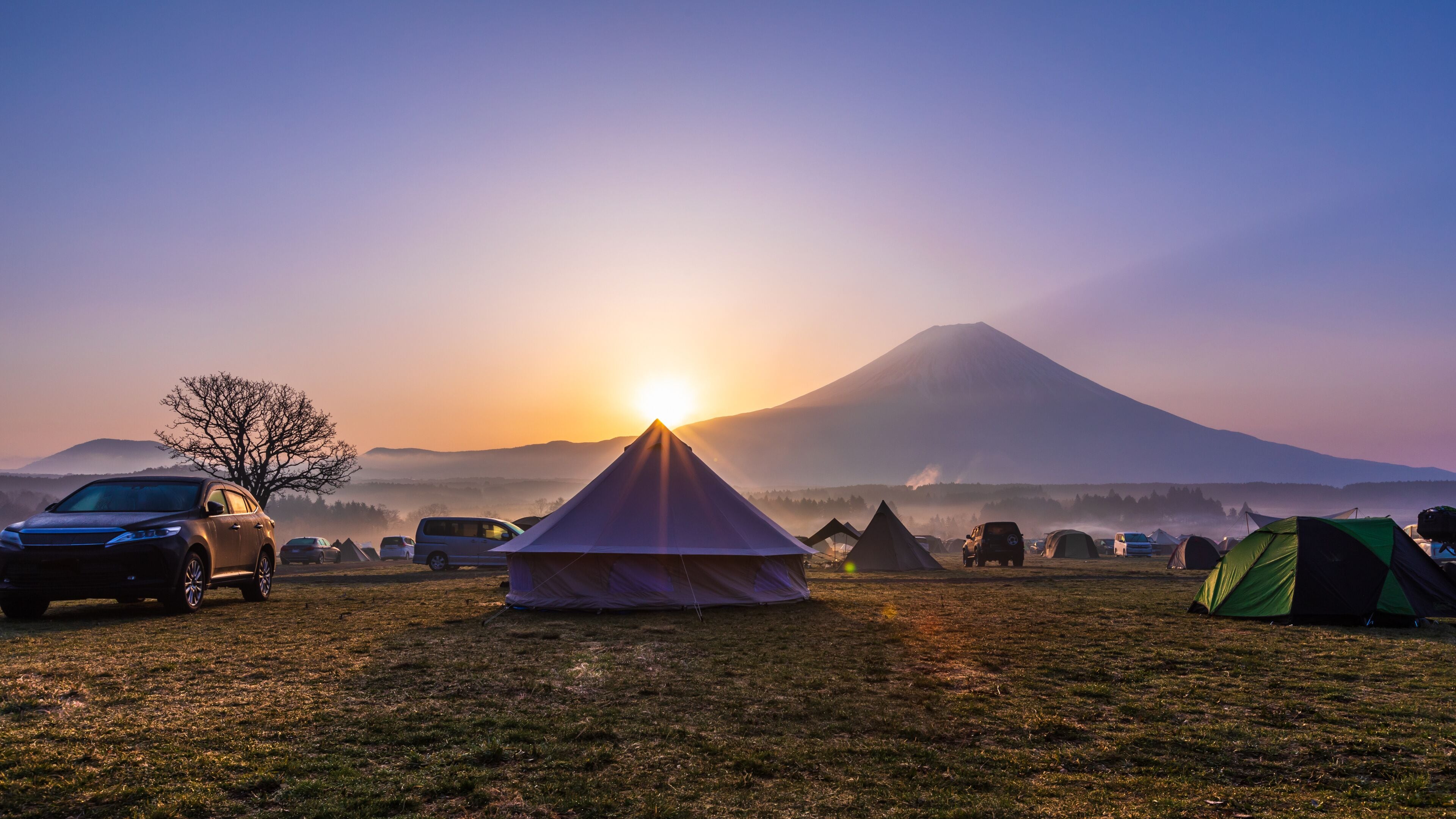 A campsite with tents, vehicles, and a mountain in the background.