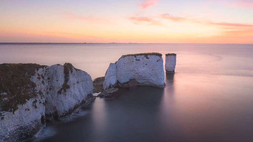 A coastal landscape with white cliffs and calm sea at sunset.