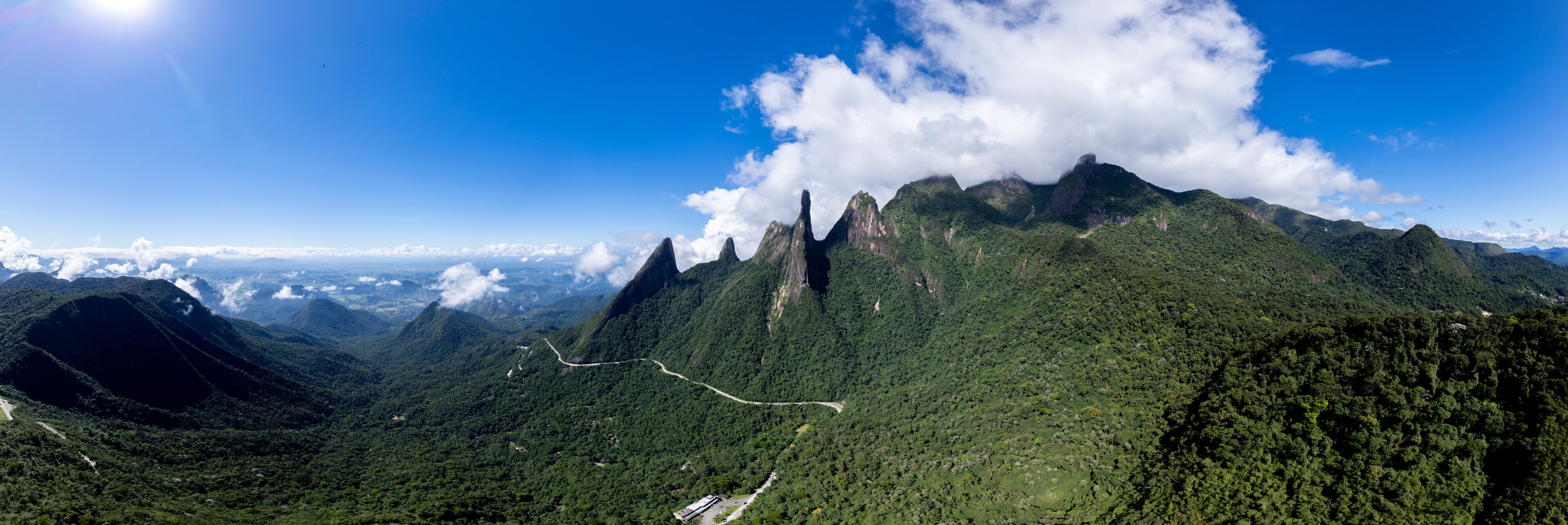 A mountainous landscape with a prominent peak, lush green forests, and a winding road.
