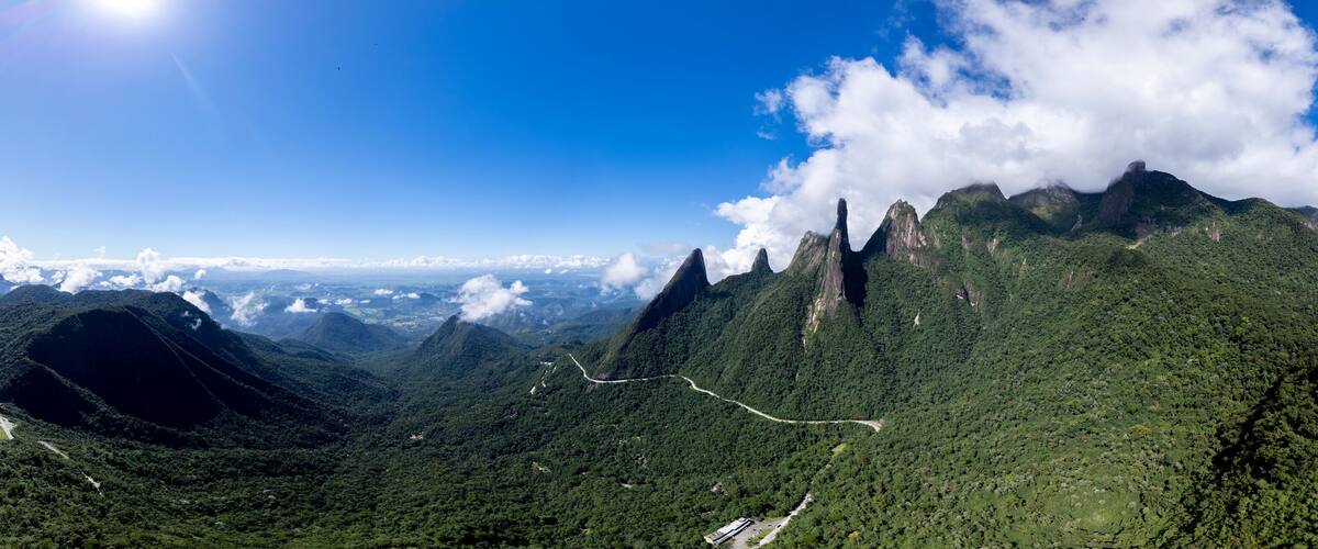 A mountainous landscape with a prominent peak, lush green forests, and a winding road.