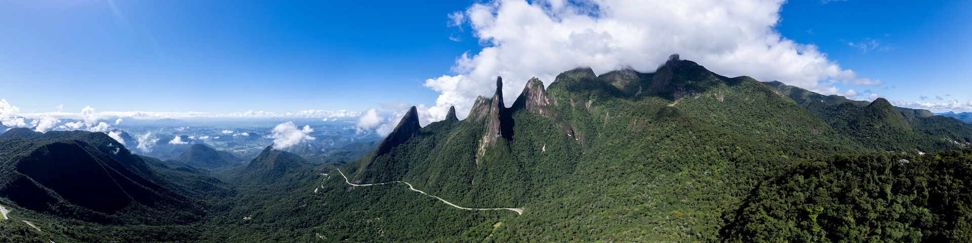 A mountainous landscape with a prominent peak, lush green forests, and a winding road.