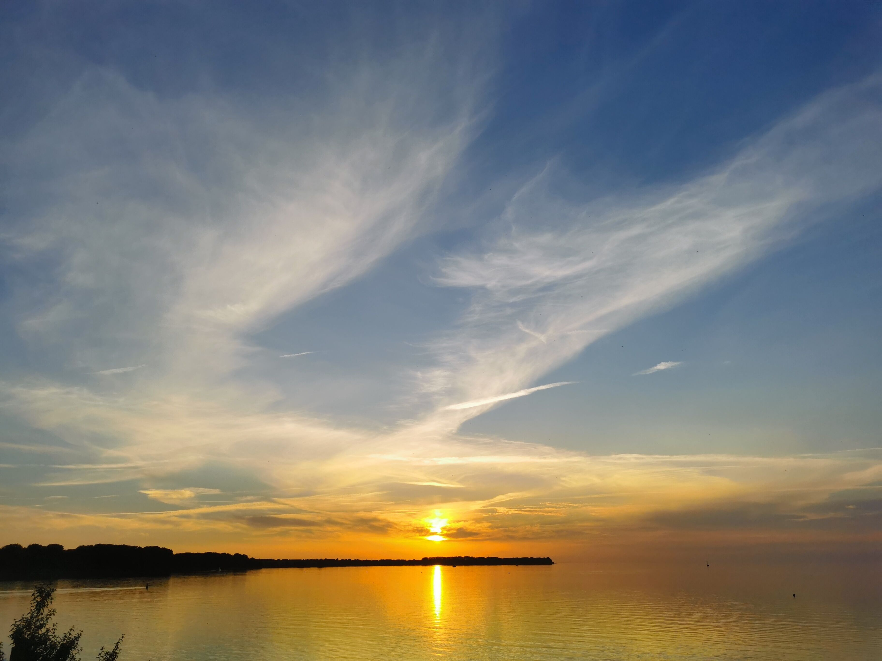 A sunset over a calm lake with a distant shoreline silhouetted against the sky.