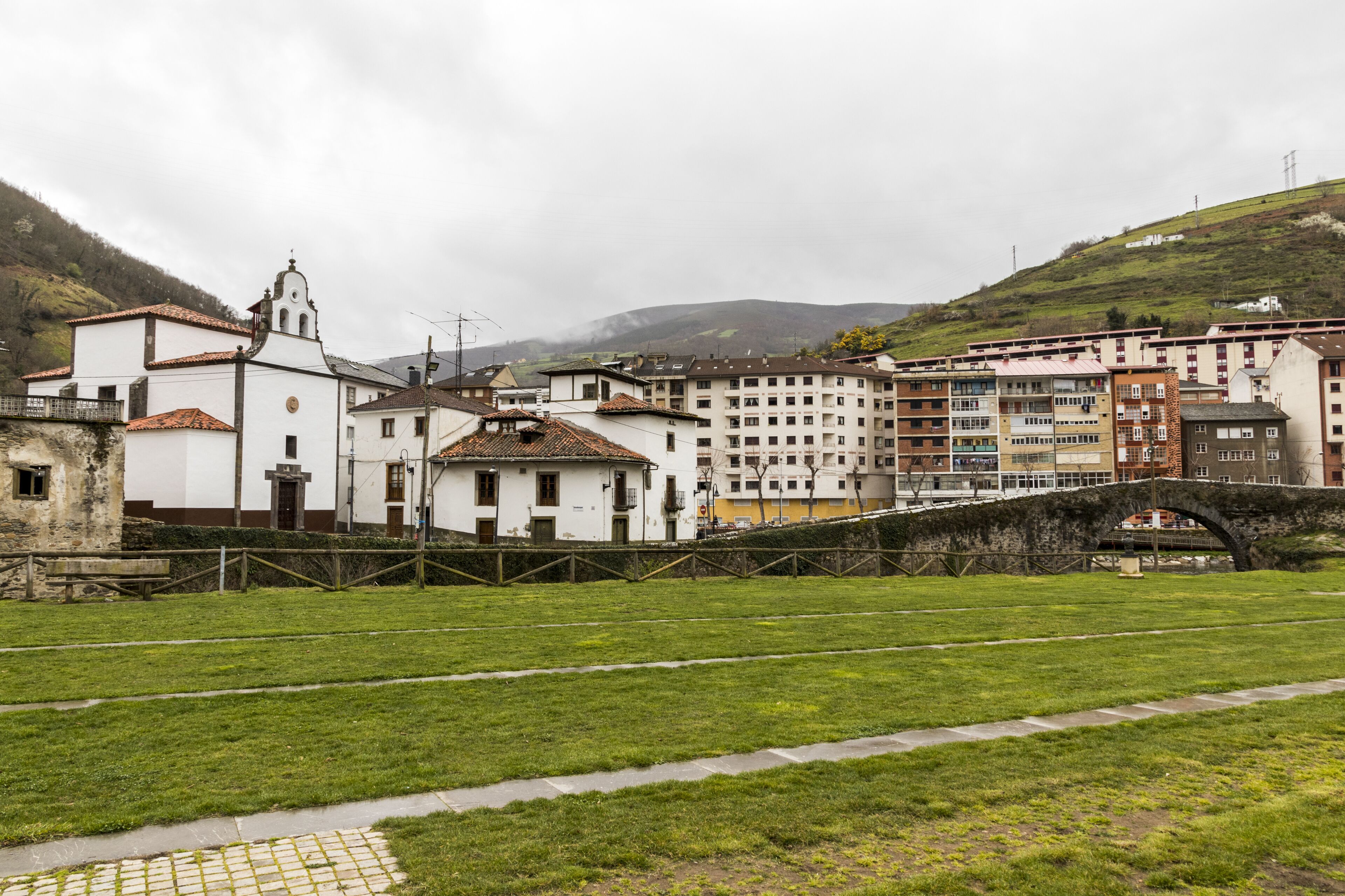 A historic town with a prominent white church, a stone bridge, and lush green hills in the background.