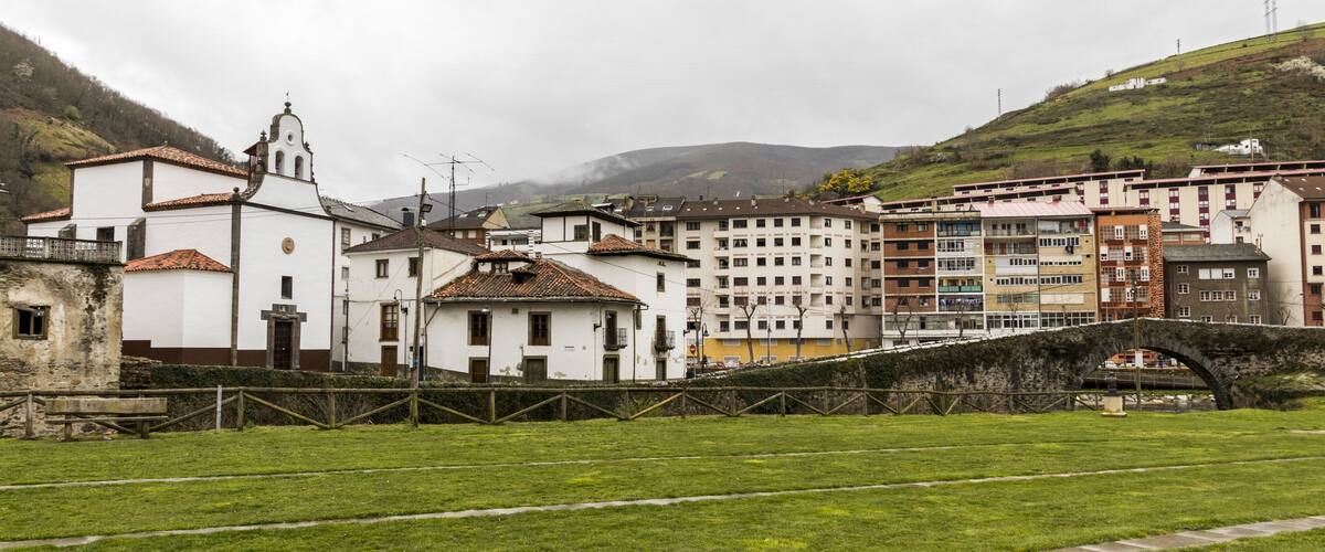 A historic town with a prominent white church, a stone bridge, and lush green hills in the background.