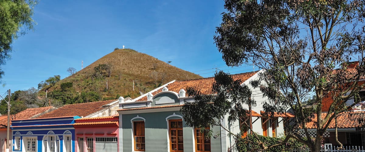 A street with colorful houses, a hill with a cross, and a clear blue sky.