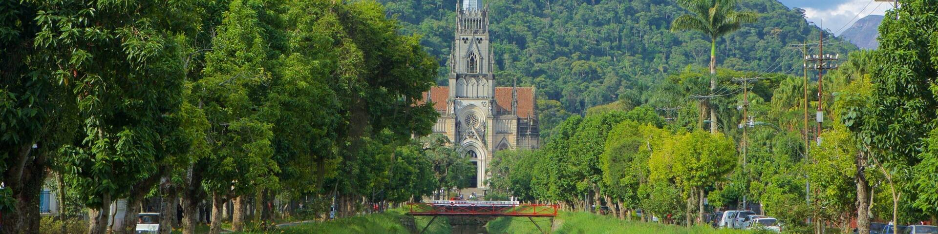 A river with a bridge, a church with a tall spire, and a forested hill in the background.