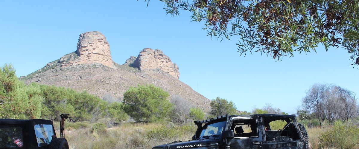 Two off-road vehicles parked on a dirt road with a rocky hill in the background.