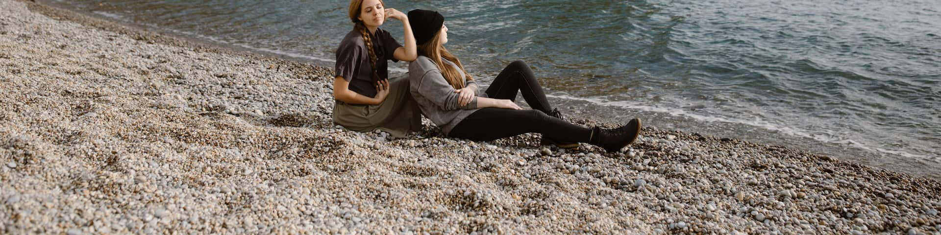 A rocky arch formation by the sea with two people sitting on the pebbly beach.