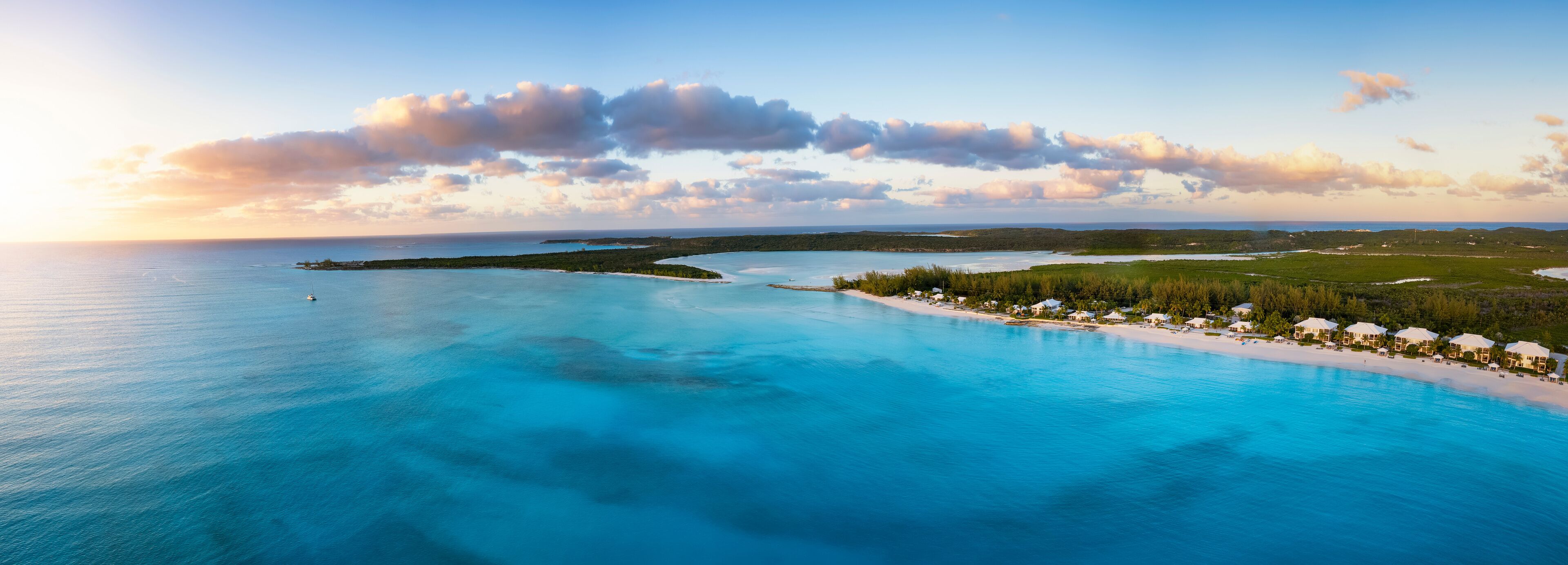 A coastal landscape with a clear blue sea, a sandy beach, and a small island with buildings.